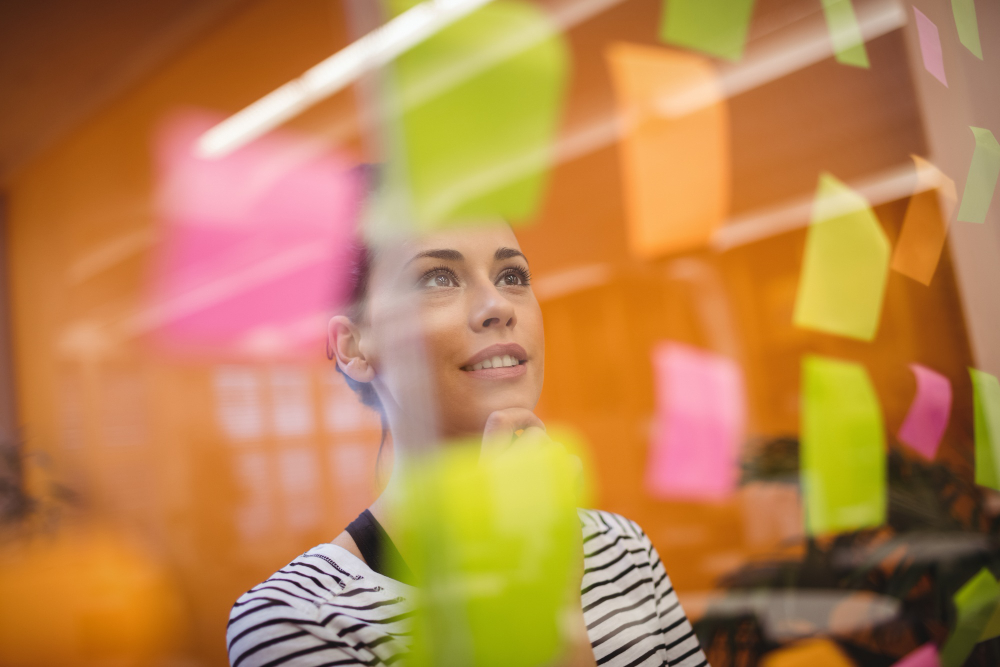 A imagem mostra uma mulher em frente a uma porta de vidro com post-its coloridos.